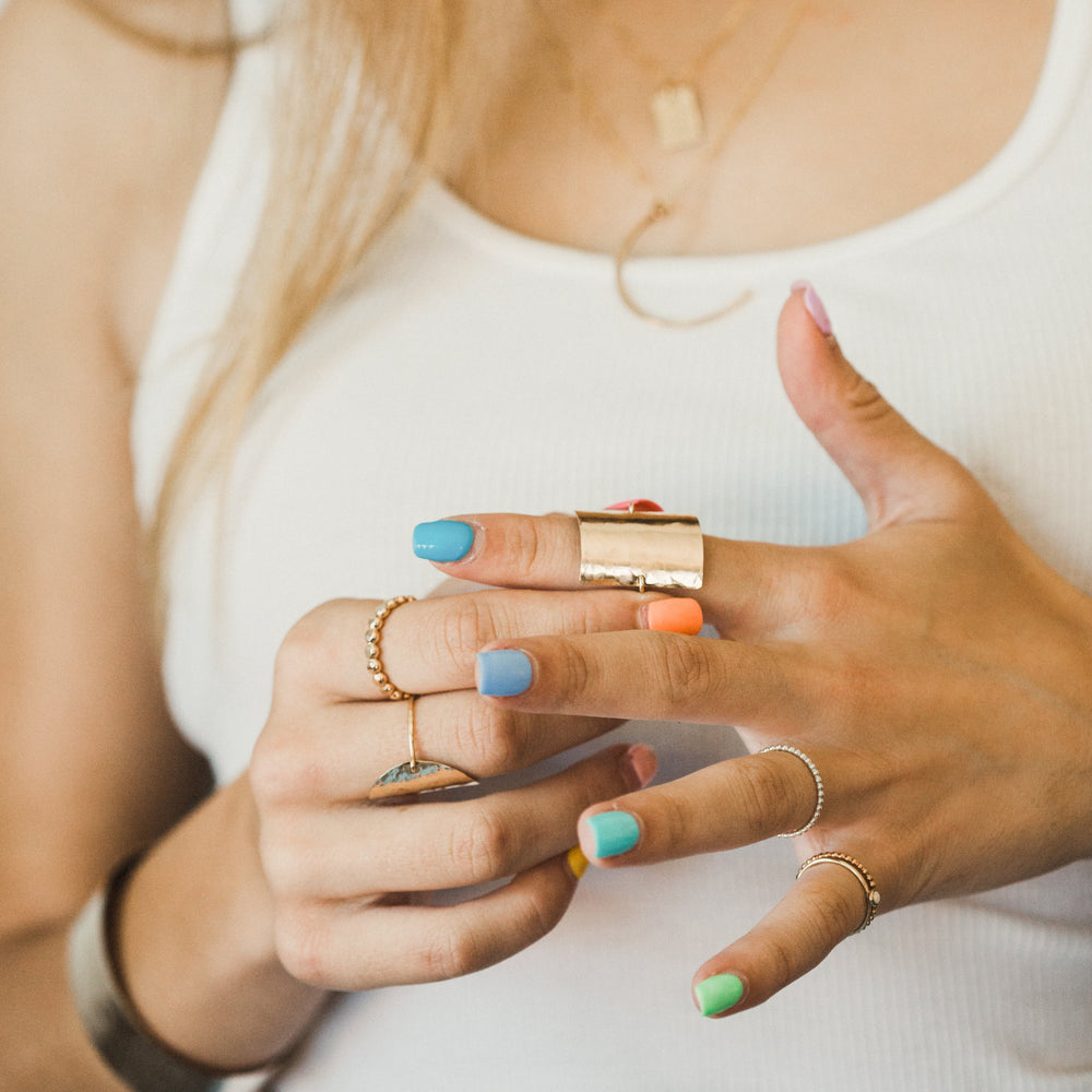 Close-up of a person holding a small rectangular shield ring with colorful nail polish on their nails.
