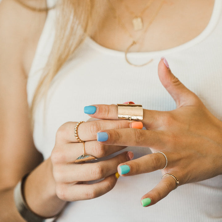 Close-up of a person holding a small rectangular shield ring with colorful nail polish on their nails.