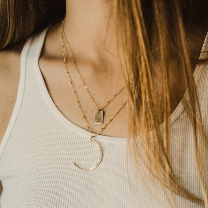 Close-up of a person wearing two gold necklaces with a plain background