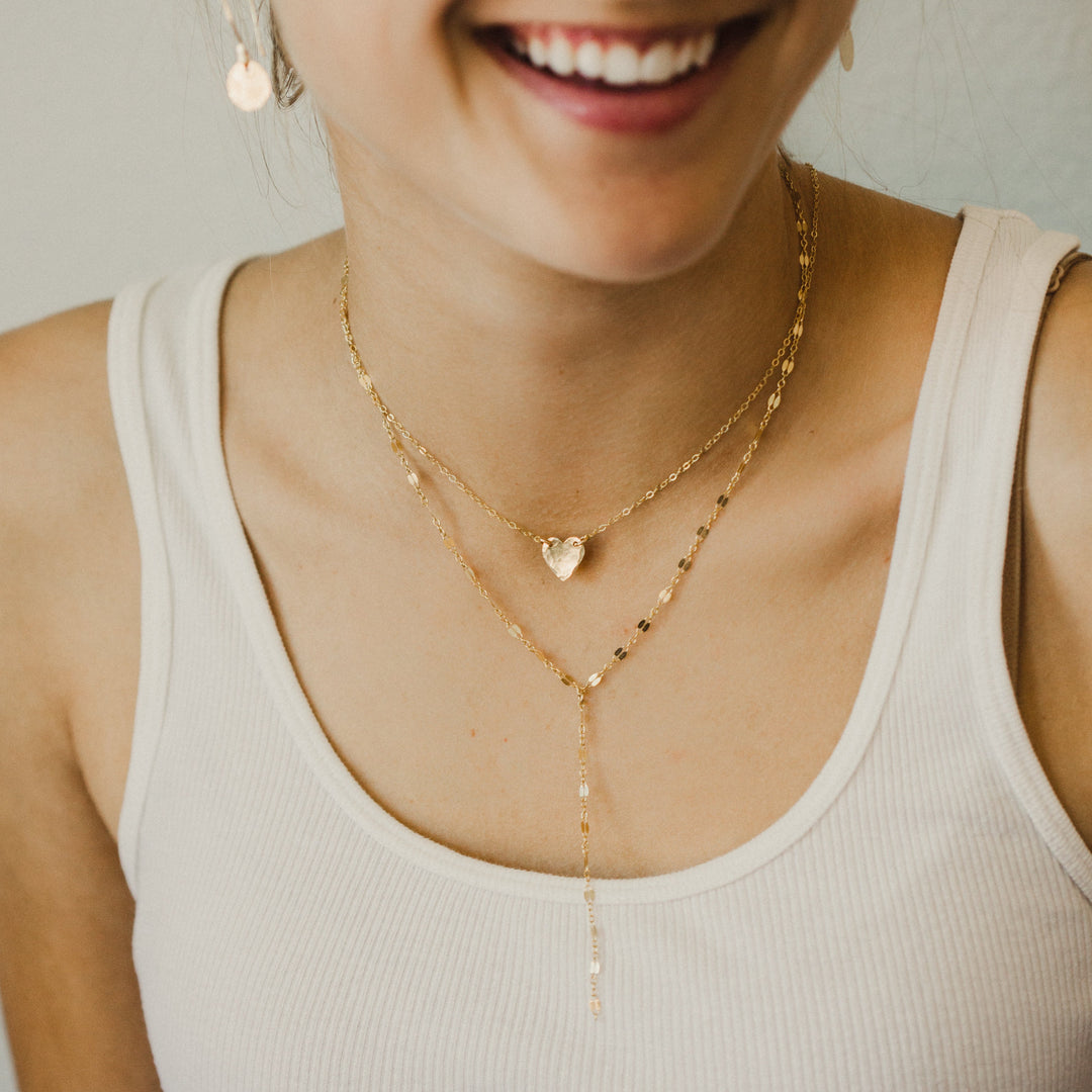 Woman wearing a white tank top and gold necklaces with a neutral background