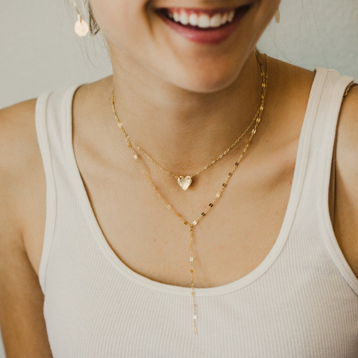 Woman wearing a white tank top and gold necklaces with a neutral background