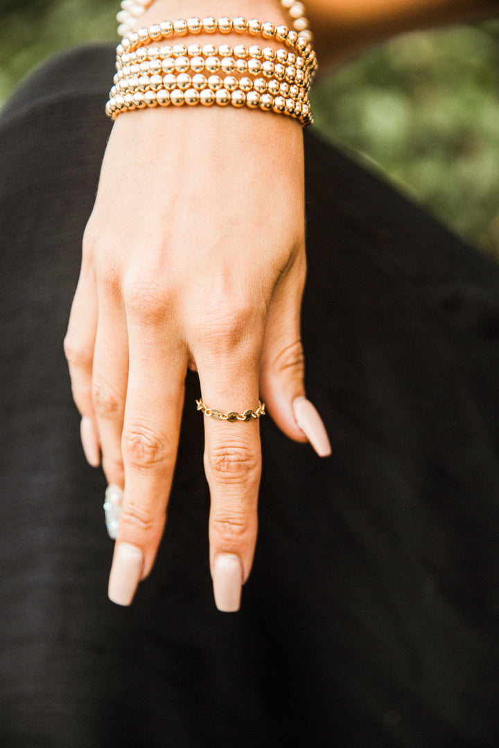 Hand with gold bracelets and gold chain ring on a blurred background