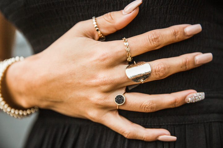 close up of women's hand with gold chain link ring, disc ring and black druzy ring