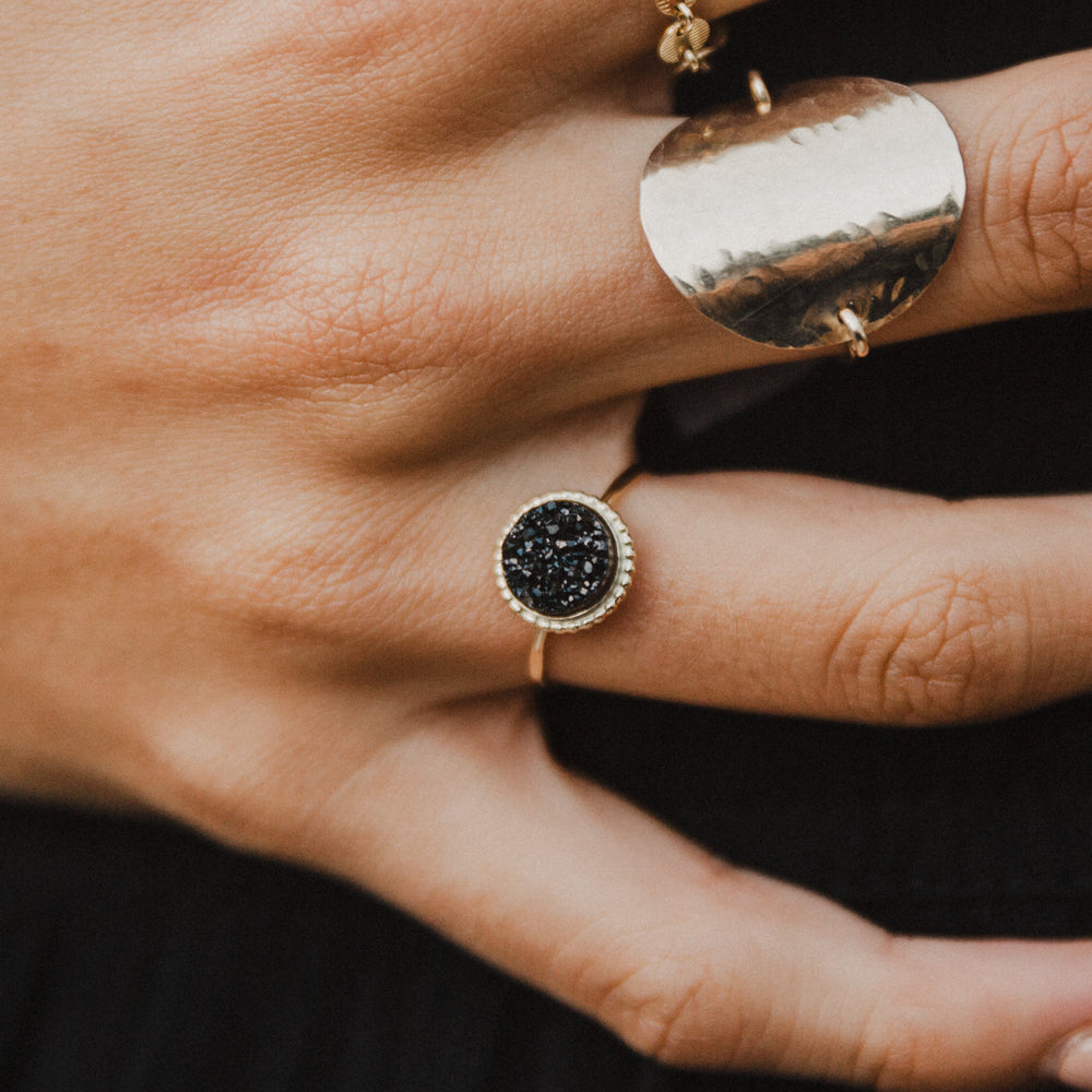 Close-up of a hand wearing black druzy gem gold rings with black gemstones on a dark background