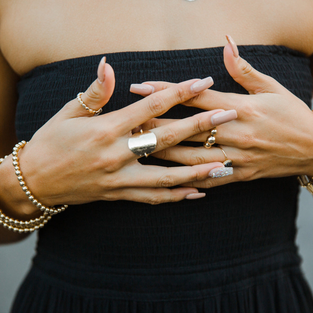Close-up of a person's hands with rings and bracelets, wearing a black strapless top.