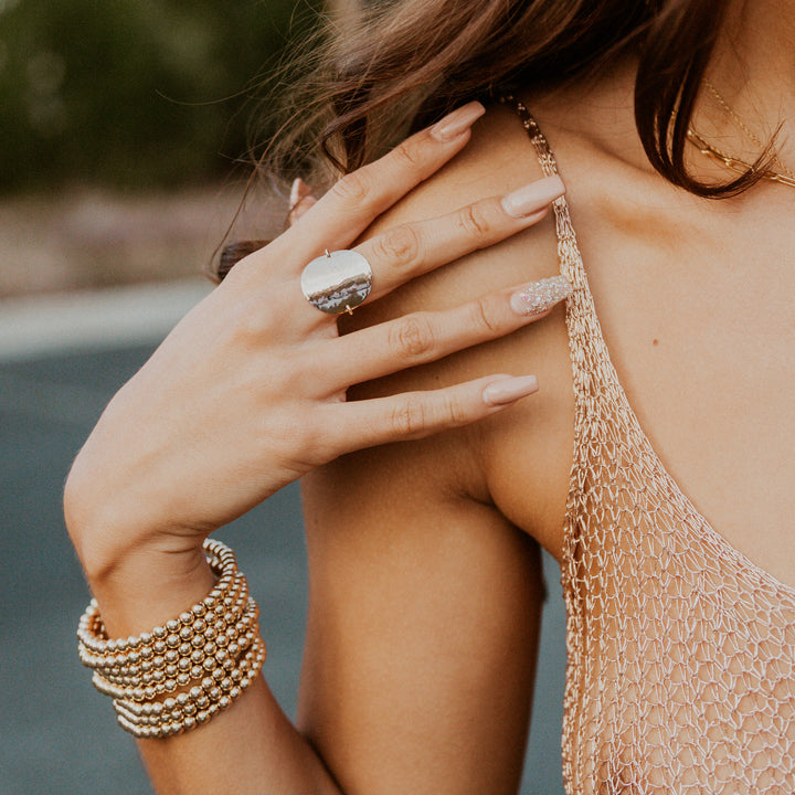 Close-up of a person wearing a gold ring and bracelet with a blurred natural background