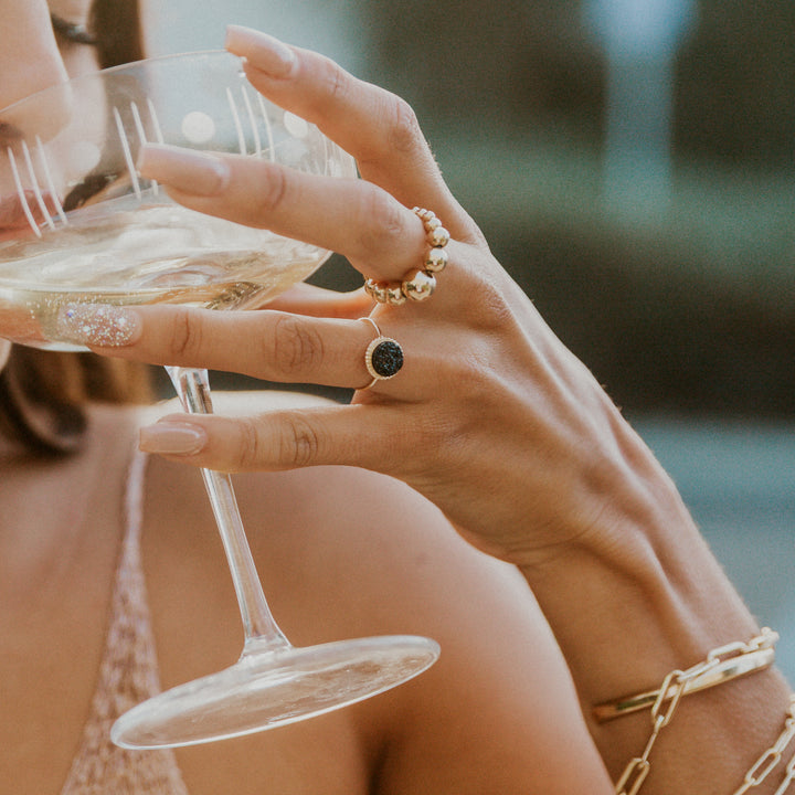 Close-up of a hand holding a glass of champagne wearing a black druzy gem gold ring