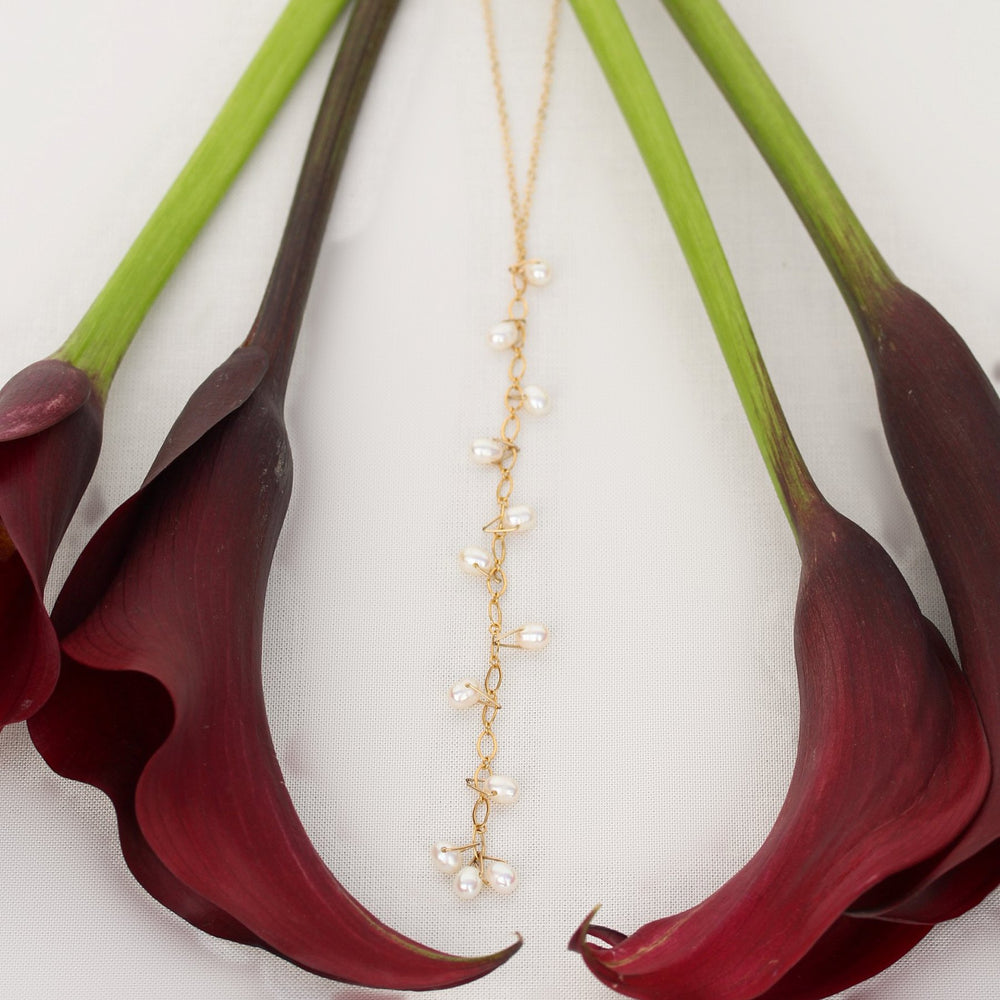 Celeste pearl Y-drop necklace in 14k gold filled chain, laid flat between burgundy calla lilies