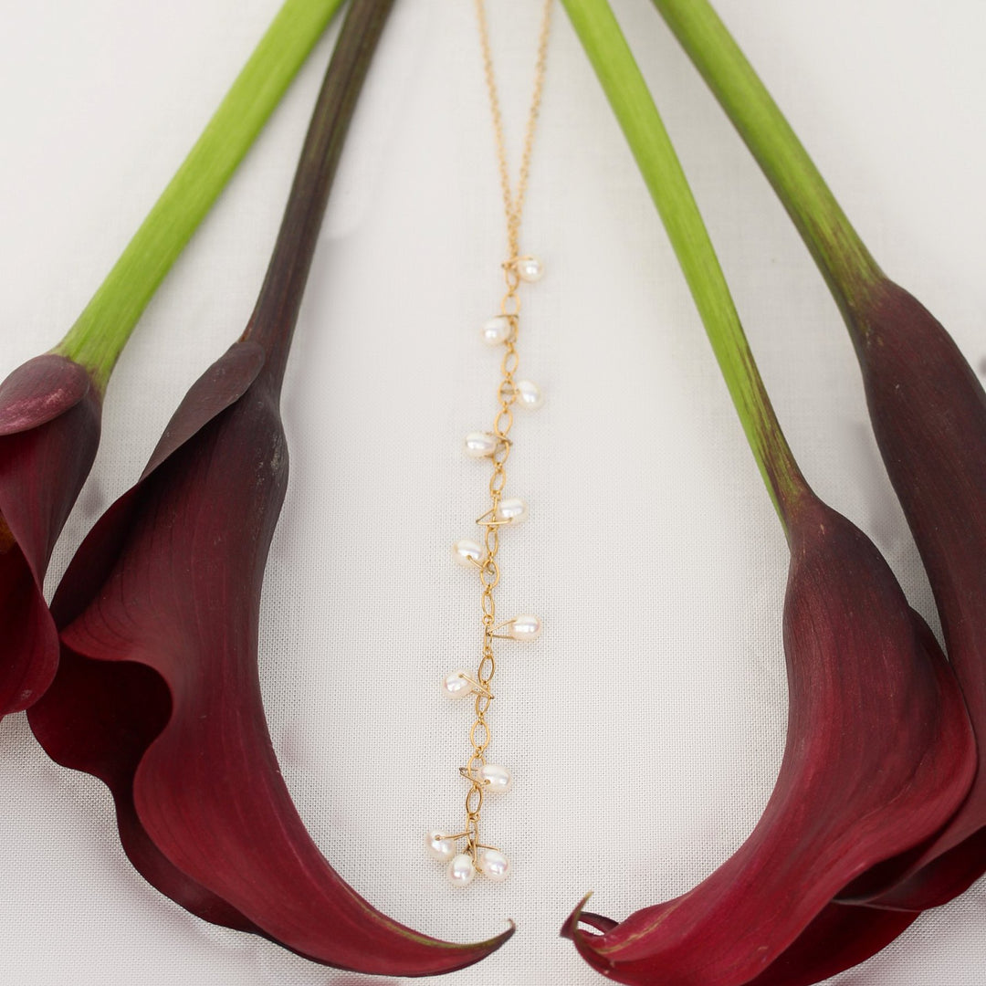 Celeste pearl Y-drop necklace in 14k gold filled chain, laid flat between burgundy calla lilies