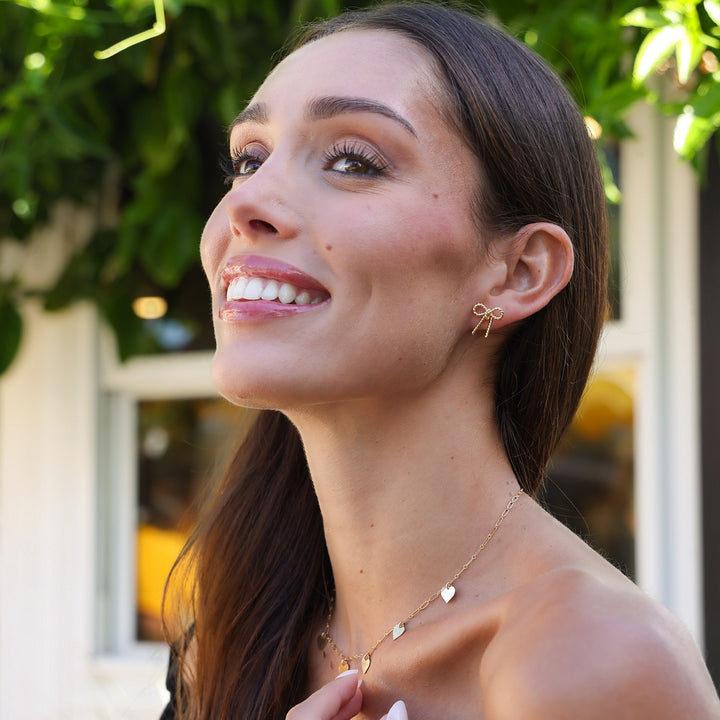 Smiling profile of a model wearing the Short Coco Bow Earring with a gold heart necklace