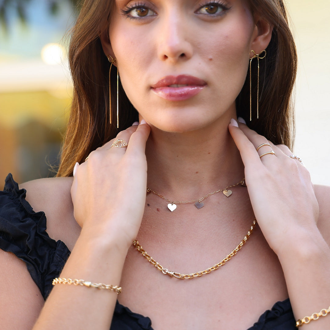 Model wearing Long Dangle Coco Bow Earrings with a gold heart charm necklace and a chunky gold chain