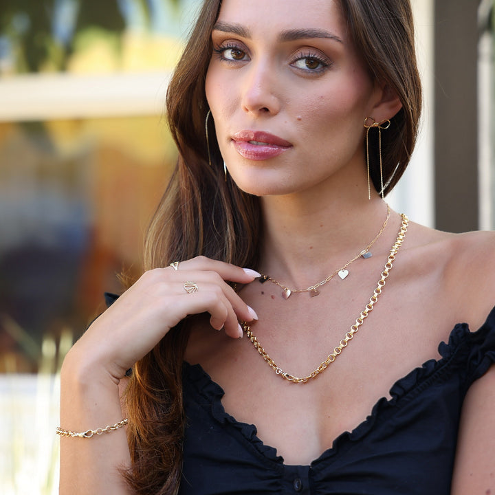 Model wearing Long Dangle Coco Bow Earrings, her hand resting near a layered gold heart necklace