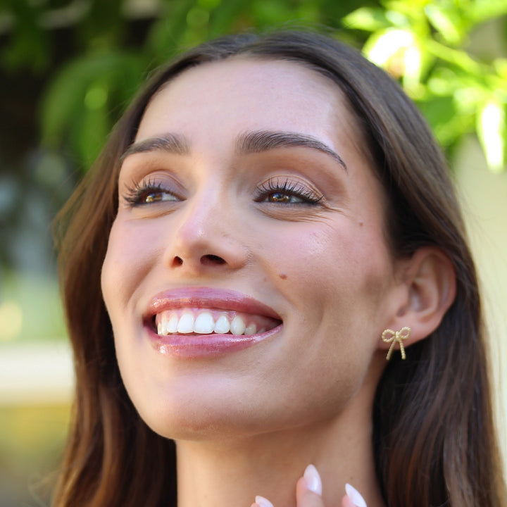 Smiling model wearing the Short Coco Bow Earring, a small twisted gold bow stud
