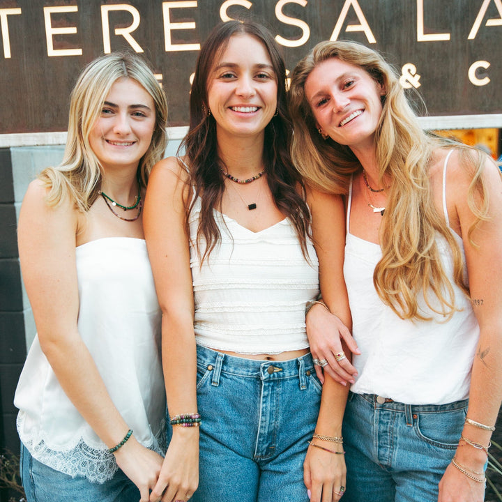 Three women wearing Teressa Lane Jewelry custom gemstone necklace Carlsbad in a stylish outdoor setting