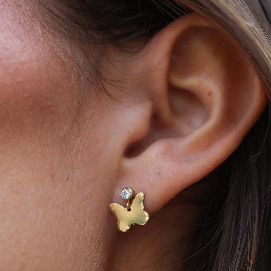 Close-up of a Dolly butterfly earring on the ear, cubic zirconia post above a hammered gold filled butterfly