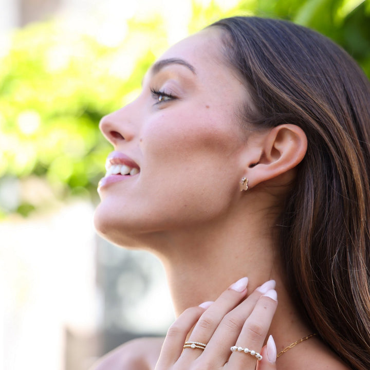 Smiling model in profile wearing the Dolly butterfly earrings with stacked gold and pearl rings
