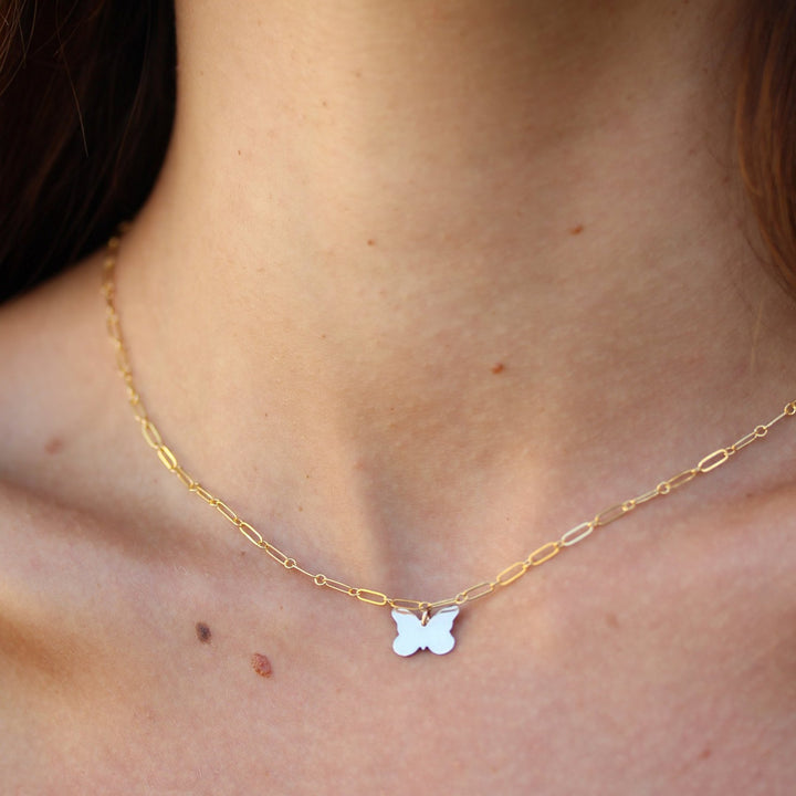 Close-up of the Dolly necklace, a small butterfly charm on fine paperclip chain worn at the base of the neck