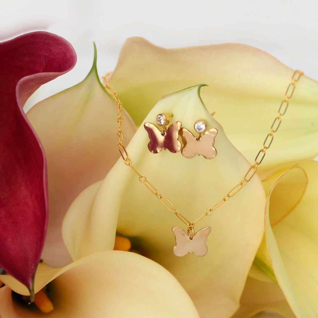Matching Dolly butterfly necklace and earrings in 14k gold filled, displayed together on cream calla lilies