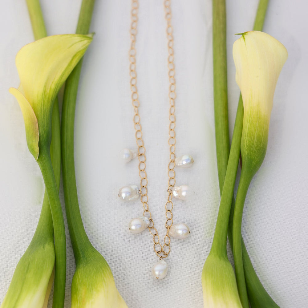 Eloise necklace with seven baroque pearl drops on 14k gold filled sparkle oval link chain, laid flat between cream calla lilies