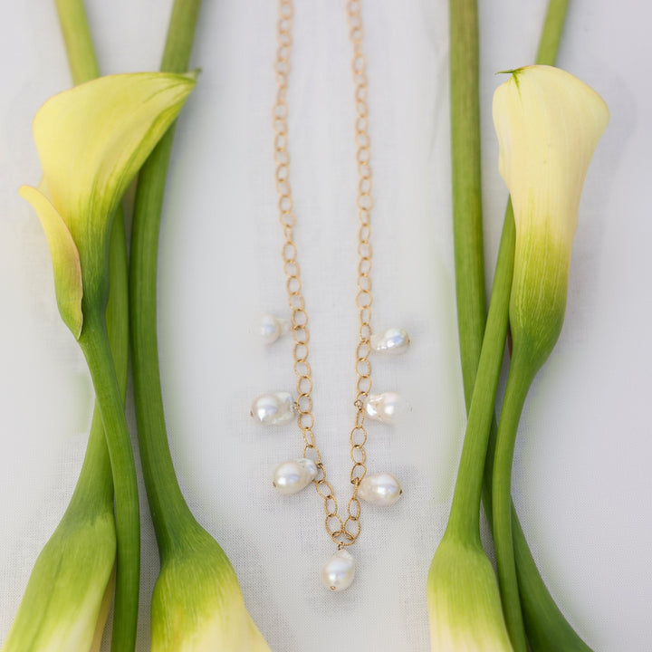 Eloise necklace with seven baroque pearl drops on 14k gold filled sparkle oval link chain, laid flat between cream calla lilies