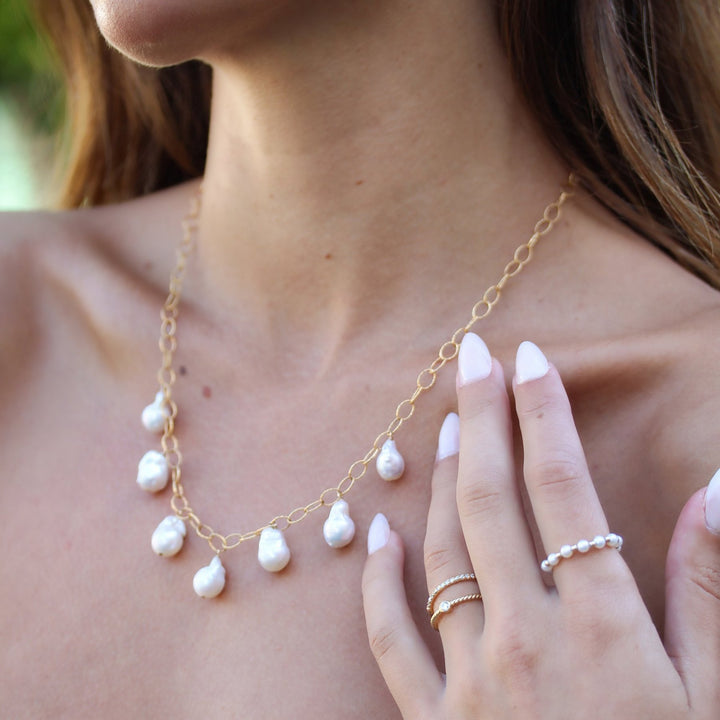 Close-up of the Eloise baroque pearl necklace on the collarbone, styled with stacked gold and pearl rings