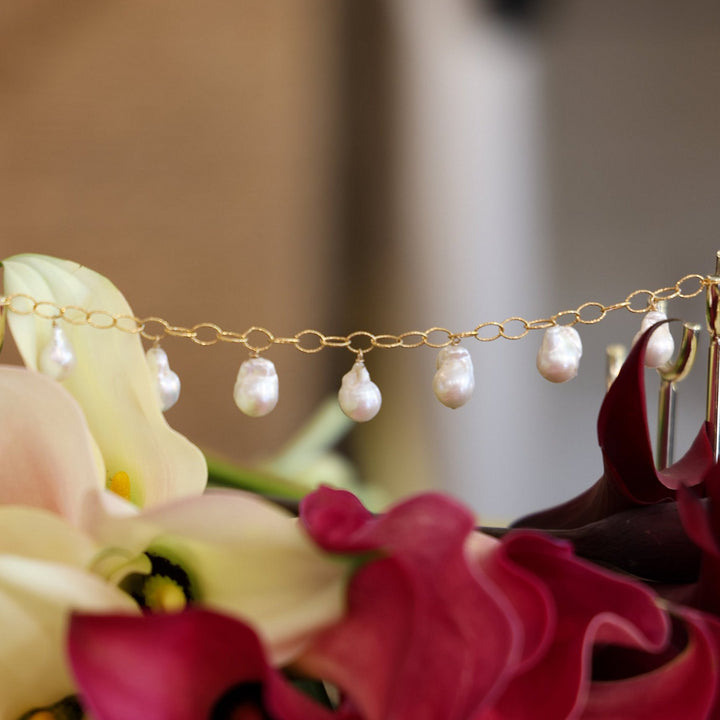 Eloise baroque pearl drops hanging from sparkle oval link chain above pink and cream calla lilies