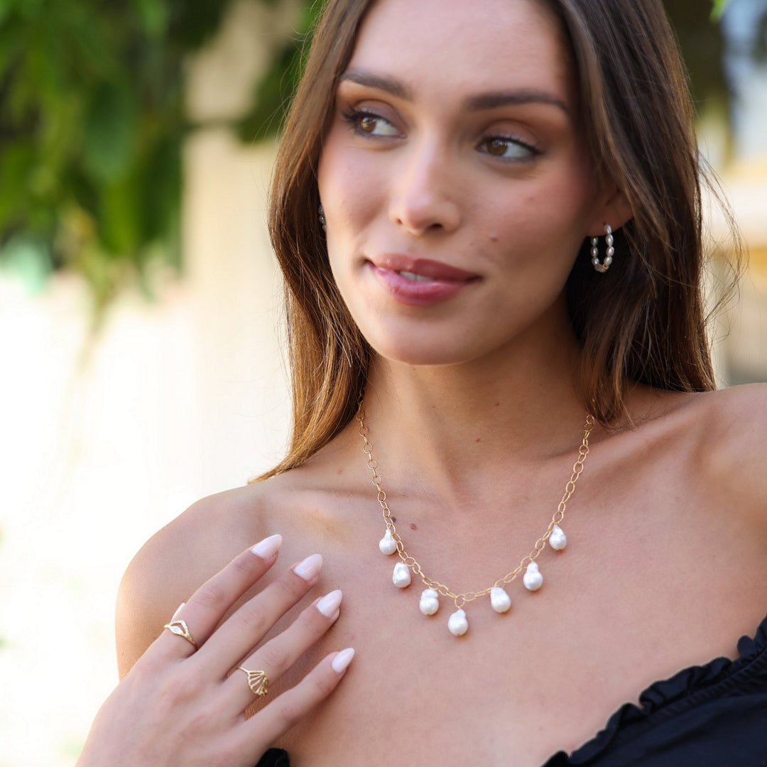 Model in an off-the-shoulder black top wearing the Eloise baroque pearl necklace with pearl hoop earrings