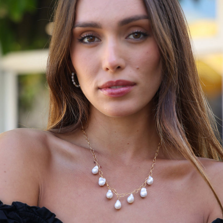 Portrait of a model wearing the Eloise gold filled baroque pearl drop necklace against garden greenery