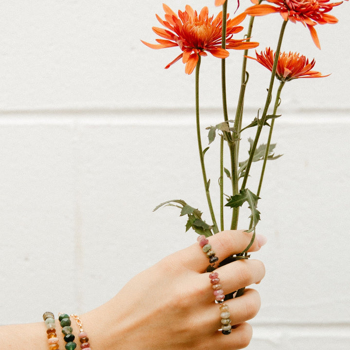 Hand holding flowers while wearing an Emma gemstone ring and beaded bracelets from Teressa Lane Jewelry