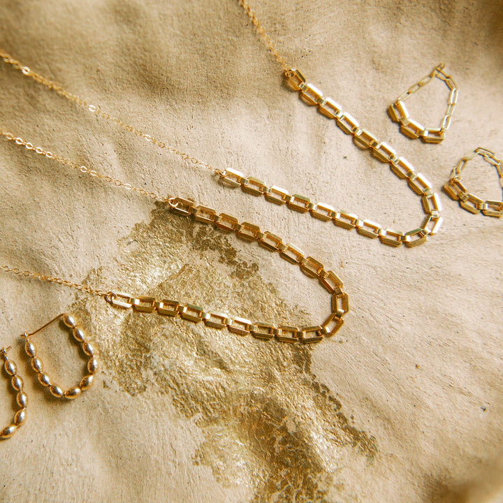 Farrah gold necklace styled with matching gold earrings on a textured surface
