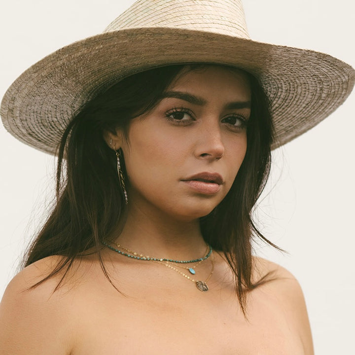 Woman wearing Teressa Lane Jewelry gold disc necklace for women with layered turquoise beads and wide straw hat