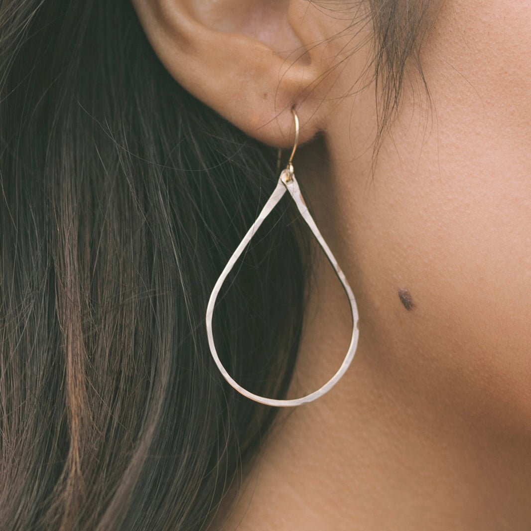 Close-up of gold Lei earrings by Teressa Lane Jewelry worn on an ear with long dark hair