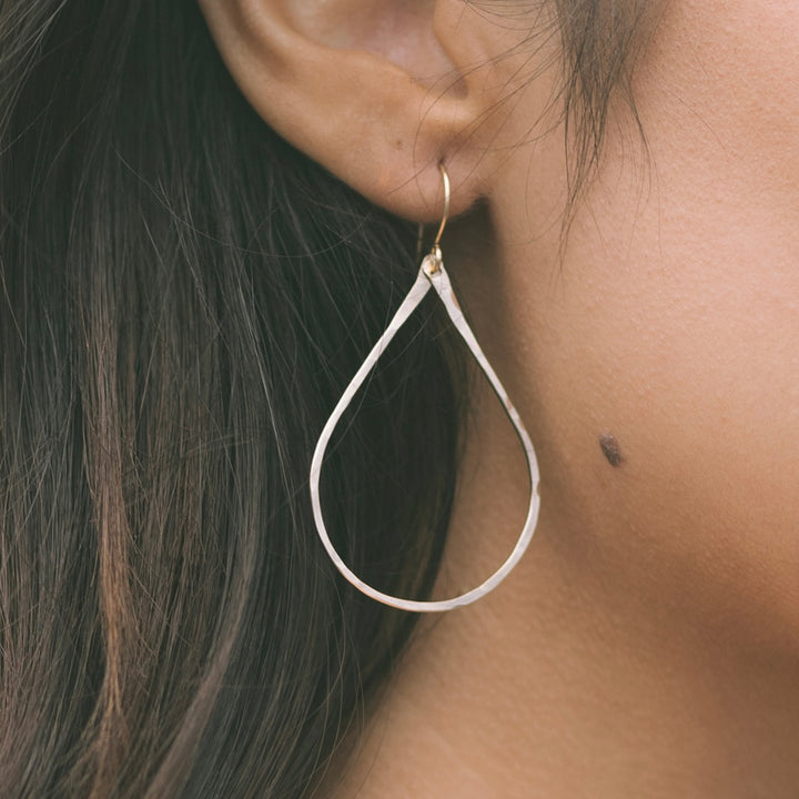 Close-up of gold Lei earrings by Teressa Lane Jewelry worn on an ear with long dark hair