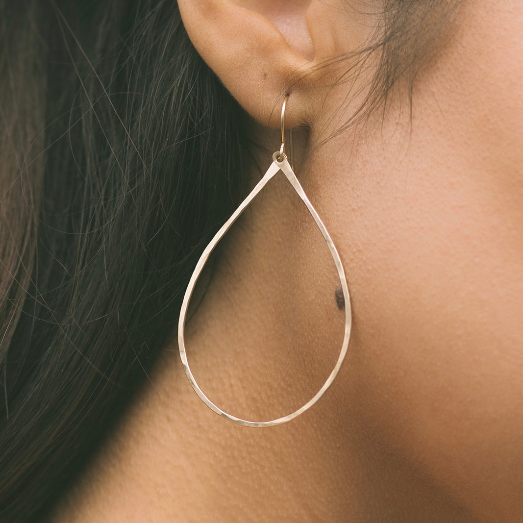 Close-up of gold Lei earrings by Teressa Lane Jewelry worn on a woman's ear with dark hair