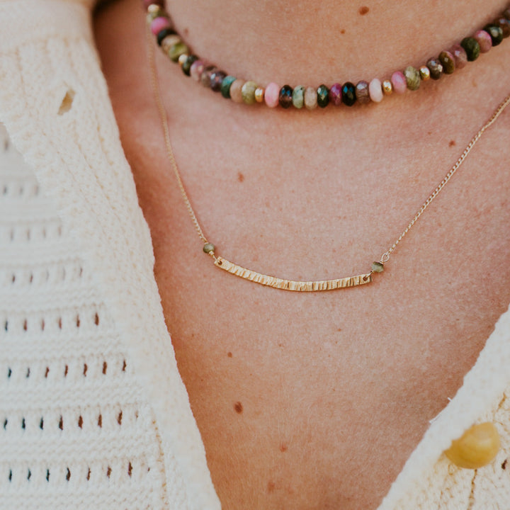 Teressa Lane Jewelry handmade gold bar necklace showcased on a model with a colorful beaded necklace