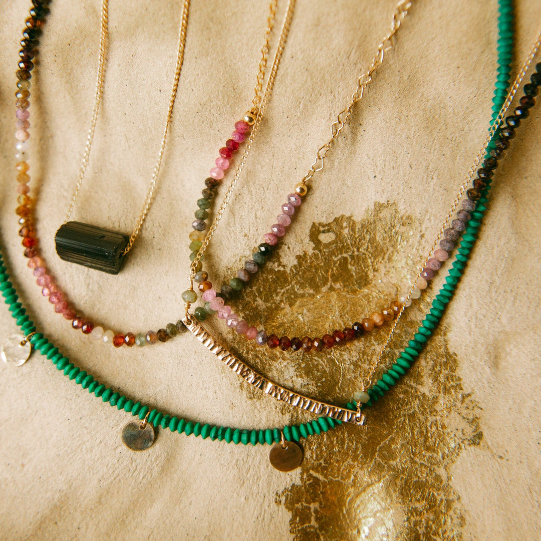 Variety of necklaces including a handcrafted piece, showcasing a handmade gold bar necklace among colorful beads
