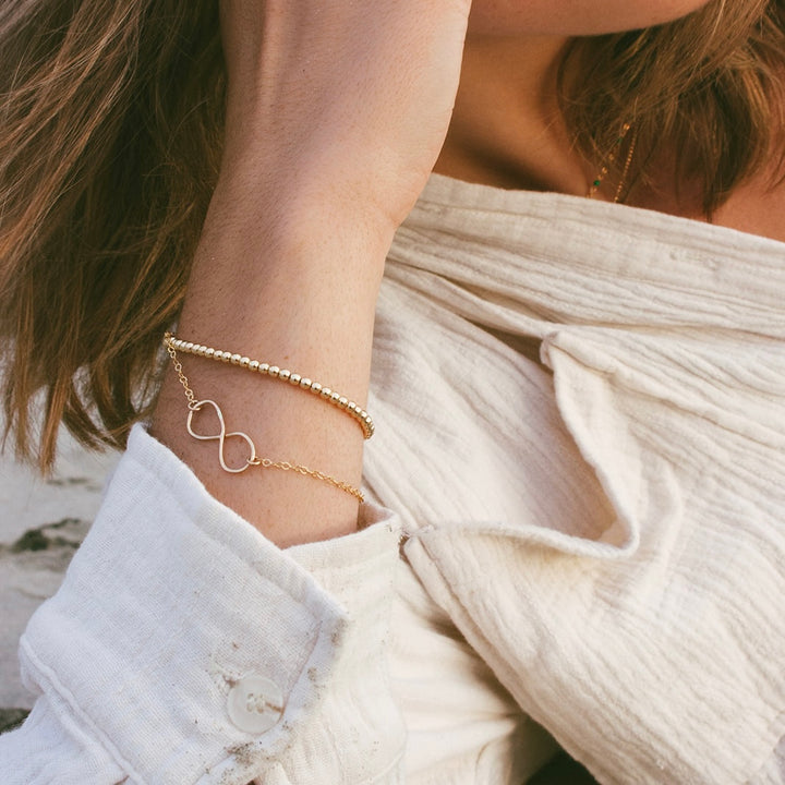 Teressa Lane Jewelry gold infinity bracelet for women worn with beaded bracelet on wrist