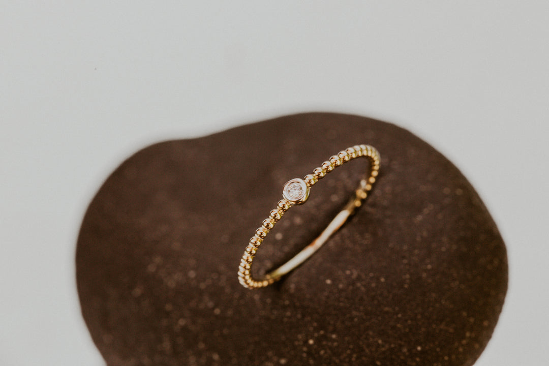 14k gold ring with a small diamond on a brown textured surface