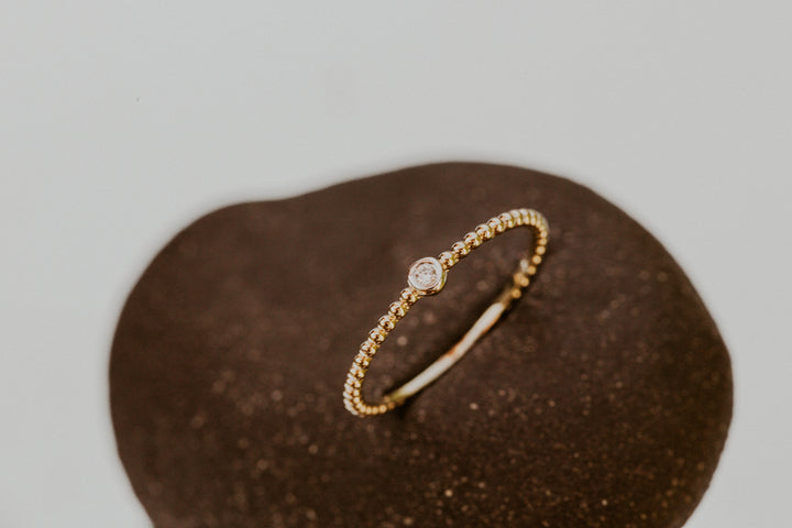 14k gold ring with a small diamond on a brown textured surface