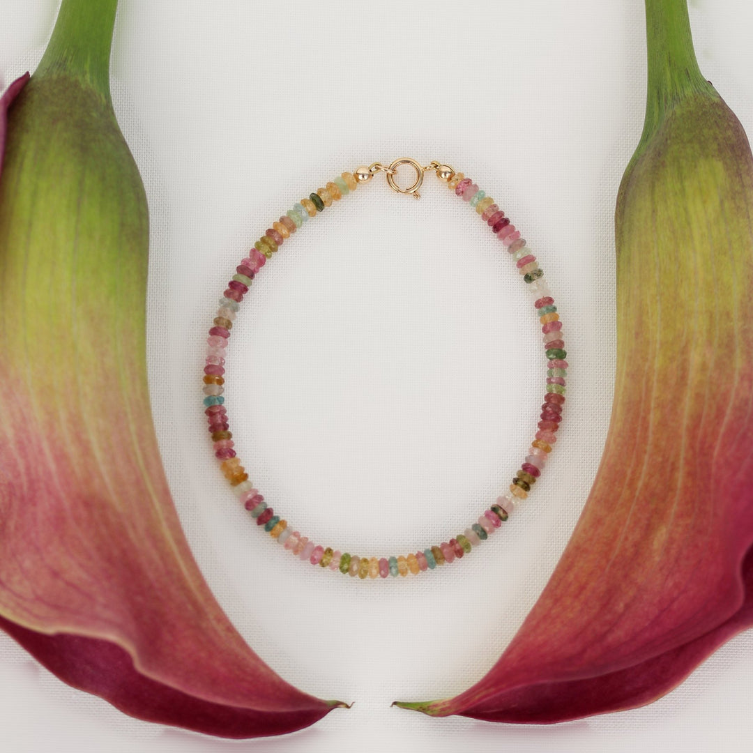 Beaded Joy bracelet of faceted multicolor tourmaline heishi beads with a gold filled spring ring clasp, framed by pink calla lilies