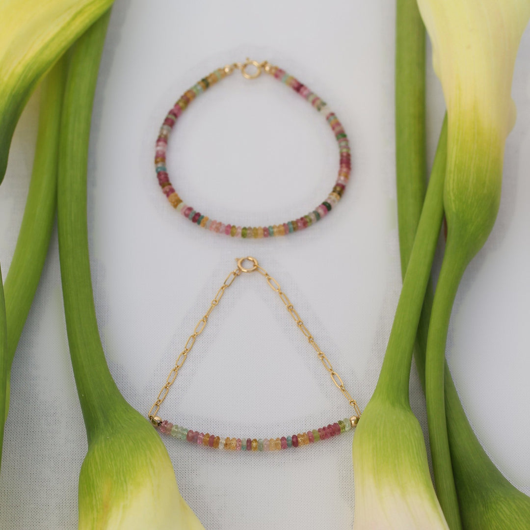 Both Joy bracelet styles, beaded and chain, laid flat together between calla lily stems