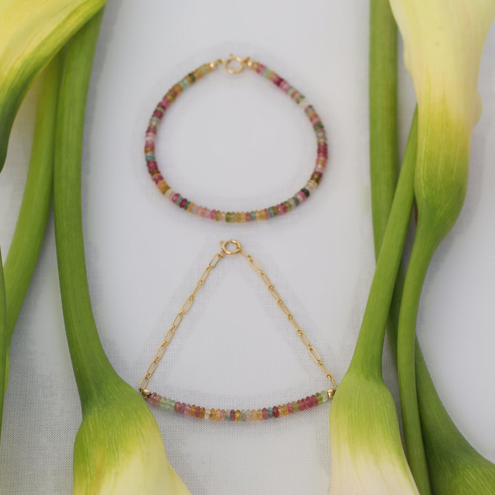 Both Joy bracelet styles, beaded and chain, laid flat together between calla lily stems