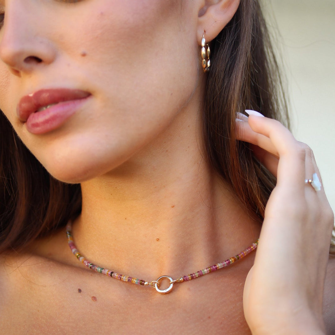 Model looking down wearing the Joy multicolor tourmaline beaded necklace with gold hoop earrings
