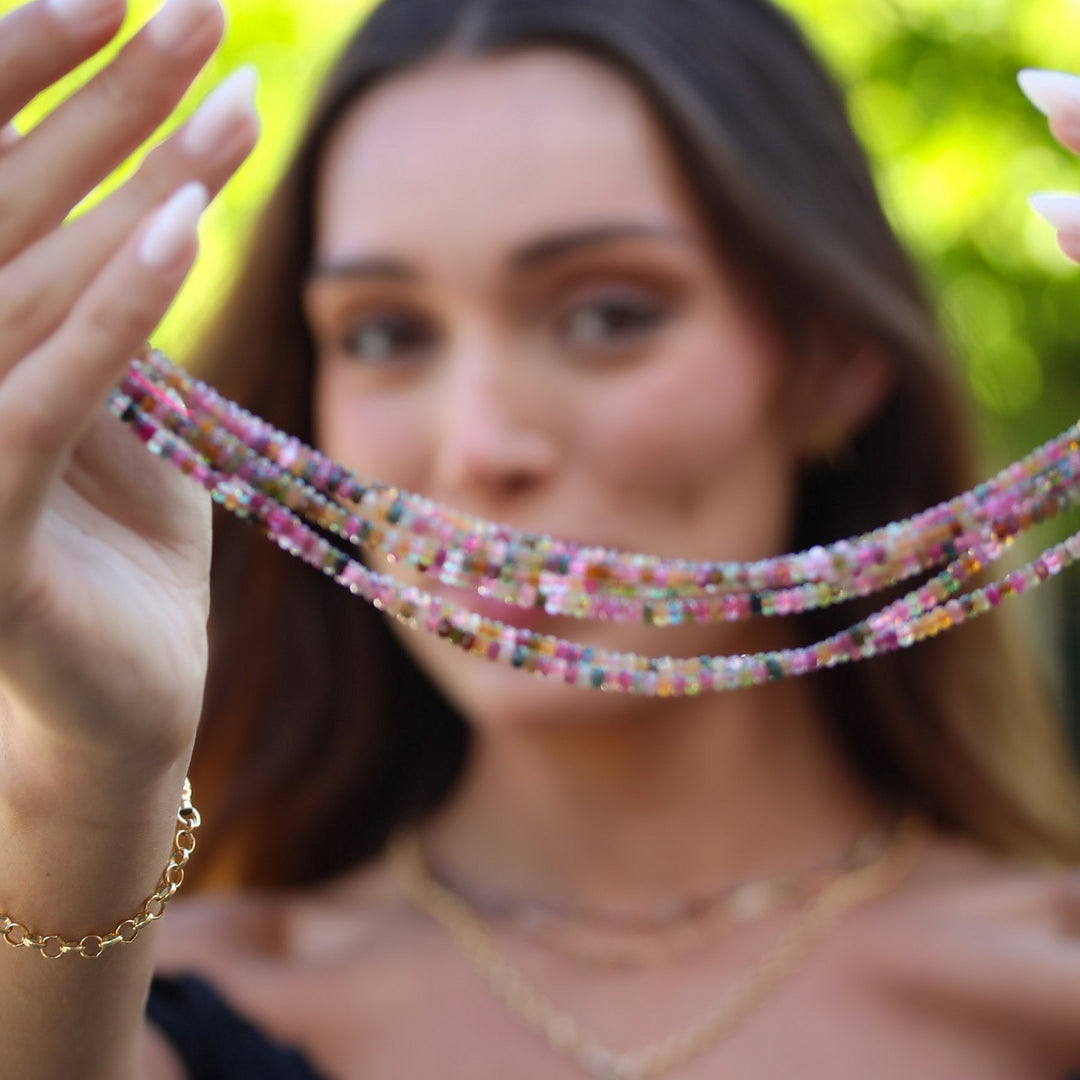 Model holding up several Joy necklaces to show the pink, green and gold tones of the tourmaline beads