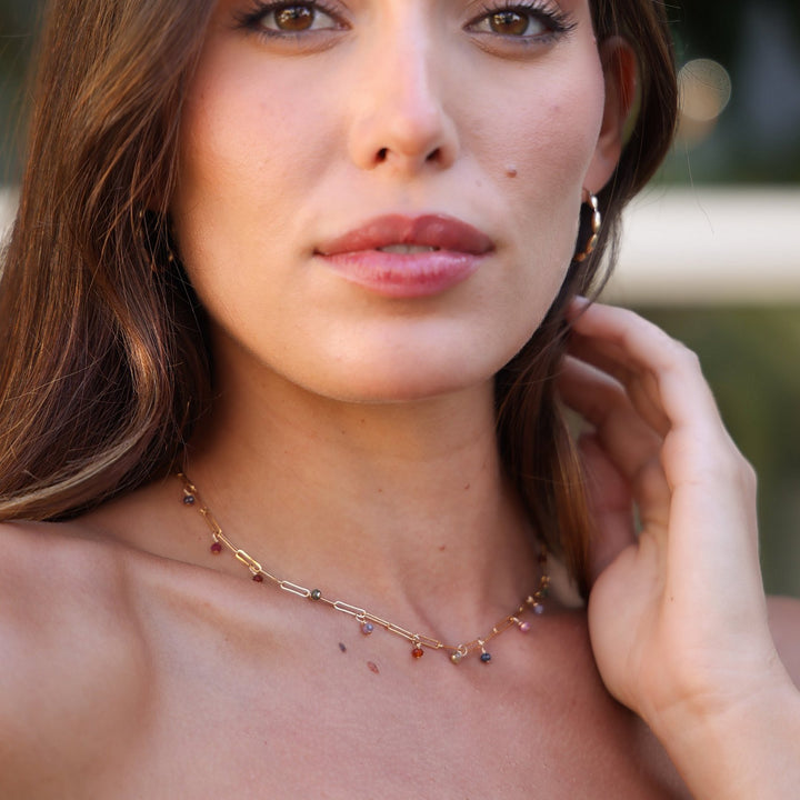 Portrait of a model wearing the gold filled Juliette spinel dangle necklace, hand at her neck
