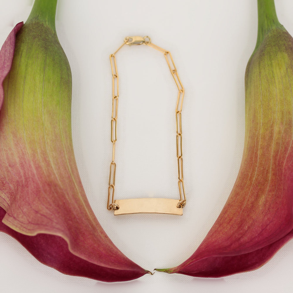 Kim bar bracelet, a hammered 14k gold filled bar on paperclip chain, framed by pink calla lilies