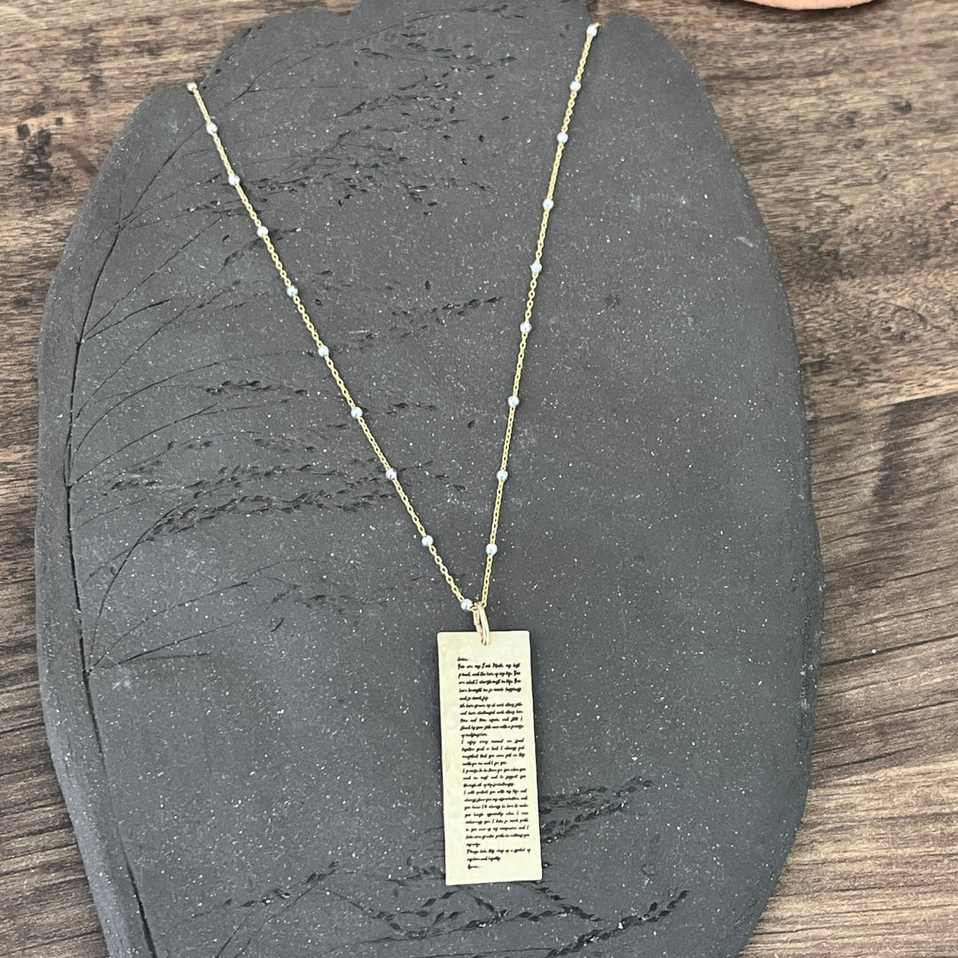 Teressa Lane Jewelry personalized gold necklace with rectangular pendant and delicate chain on black stone
