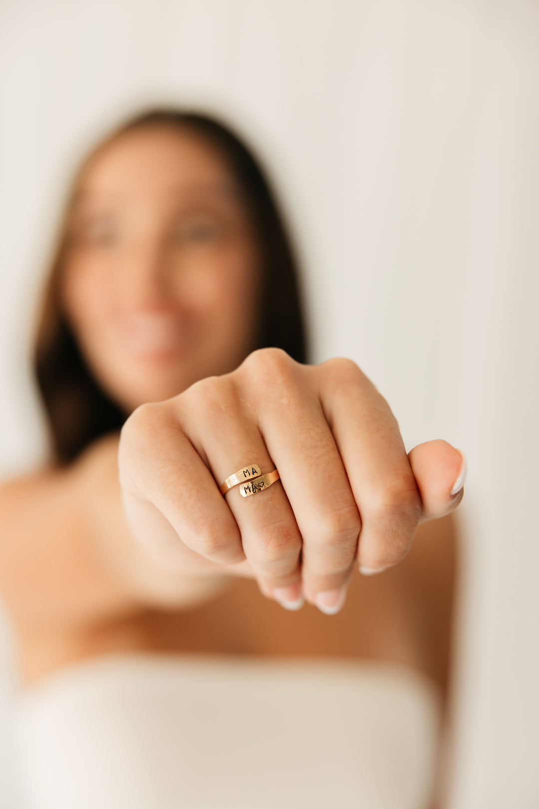 Woman's hand wearing a gold adjustable warp ring with a blurred background