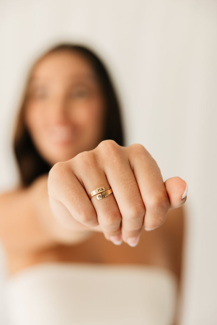 Woman's hand wearing a gold adjustable warp ring with a blurred background
