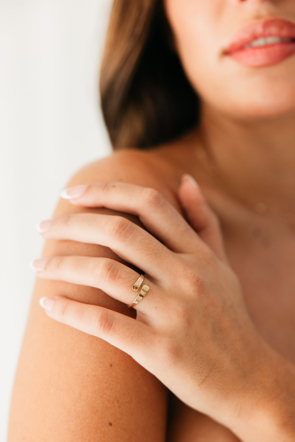 Close-up of a hand wearing a gold adjustable wrap ring on a blurred background